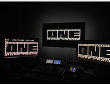 Тъмно помещение за видеомонтаж с три монитора на бюро, показващи графика като филмова лента и надпис „ONE MORE FRAME“. Пред тях има контролен панел с бутони и въртящи се регулатори, клавиатура и кабели.