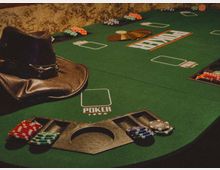 Зелена маса за покер в казино с обозначени места за играчи, отделения за чипове и централен отвор за събиране. По ръба са подредени купчини покер чипове и се виждат подплатени кожени подлакътници.