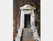 Бял вход с колони и фронтон към галерия за съвременно изкуство, до който водят няколко бетонни стъпала. Около портала има стени, обрасли със сухи лози и есенни листа.