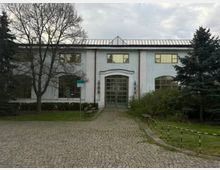 Двуетажна обществена сграда със светла фасада и метален покрив, с централен вход с големи остъклени врати и симетрично разположени прозорци. Отпред има павиран подход с пейки, ниски храсти и дървета от двете страни.