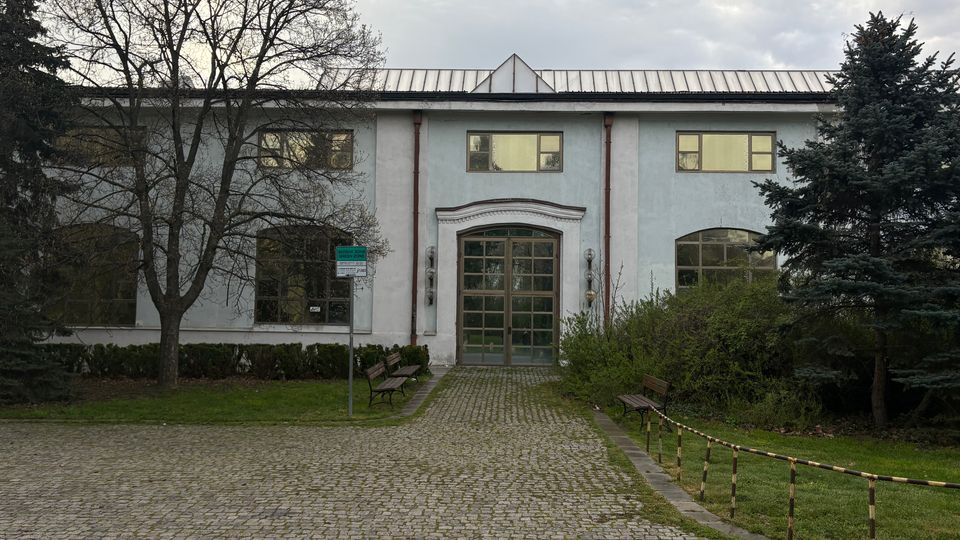 Двуетажна обществена сграда със светла фасада и метален покрив, с централен вход с големи остъклени врати и симетрично разположени прозорци. Отпред има павиран подход с пейки, ниски храсти и дървета от двете страни.
